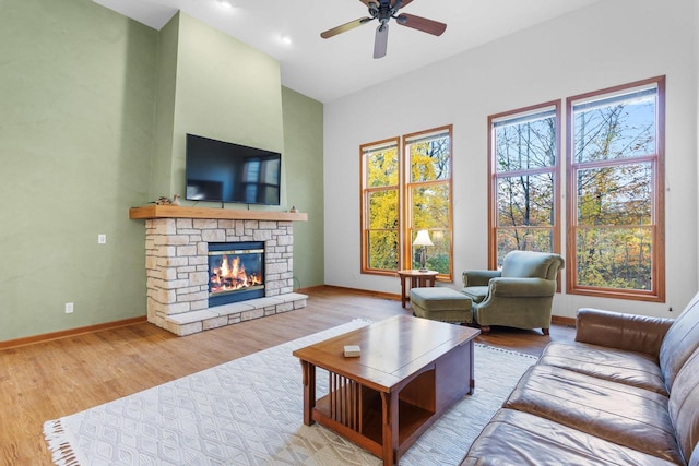 living room with a stone fireplace, light wood-type flooring, and ceiling fan