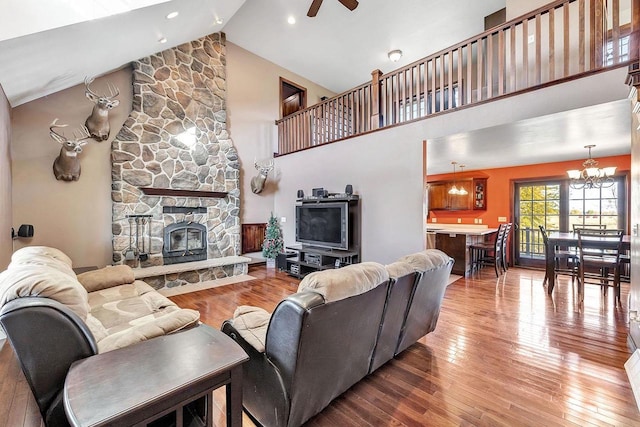 living room with light hardwood / wood-style flooring, a stone fireplace, ceiling fan with notable chandelier, and high vaulted ceiling