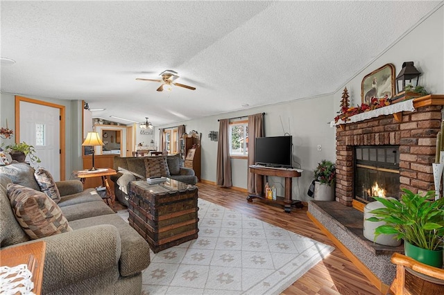 living room featuring a fireplace, vaulted ceiling, a textured ceiling, light hardwood / wood-style floors, and ceiling fan