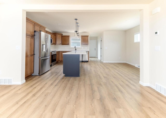 kitchen featuring pendant lighting, sink, stainless steel appliances, a center island, and light hardwood / wood-style floors