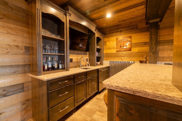 bar featuring wood ceiling, wooden walls, sink, light stone countertops, and dark brown cabinetry