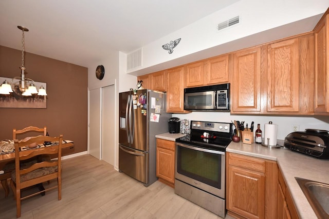 kitchen featuring sink, hanging light fixtures, stainless steel appliances, a notable chandelier, and light hardwood / wood-style flooring