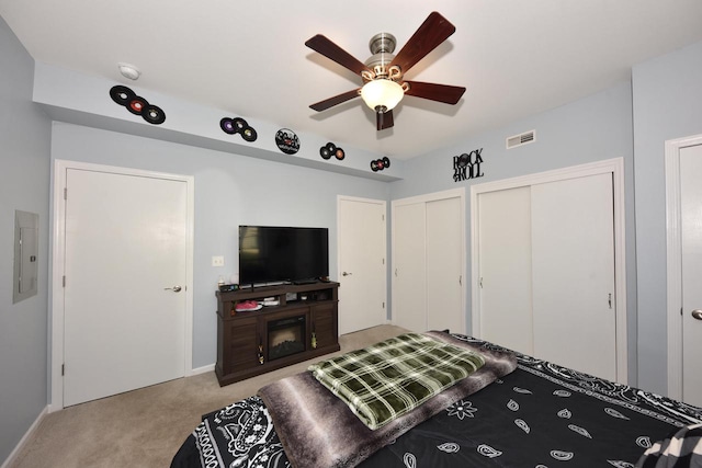 carpeted bedroom featuring electric panel, two closets, a fireplace, and ceiling fan