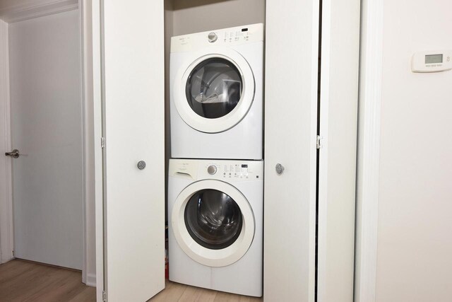 laundry room featuring stacked washer / drying machine and light hardwood / wood-style floors