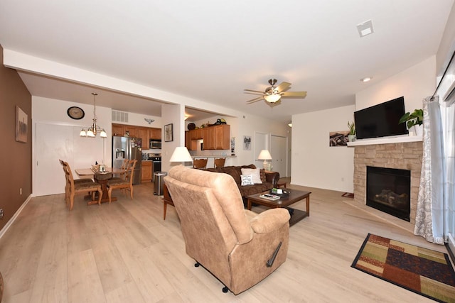 living room featuring light hardwood / wood-style flooring, ceiling fan with notable chandelier, and a fireplace