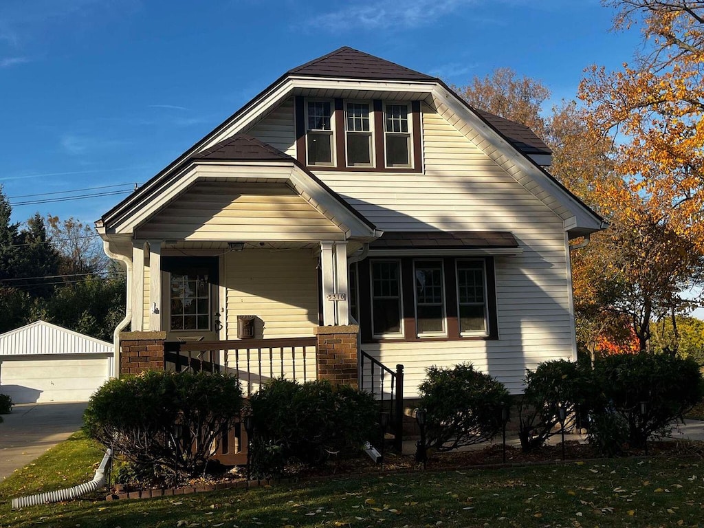 view of front facade featuring a garage, a front lawn, an outbuilding, and a porch