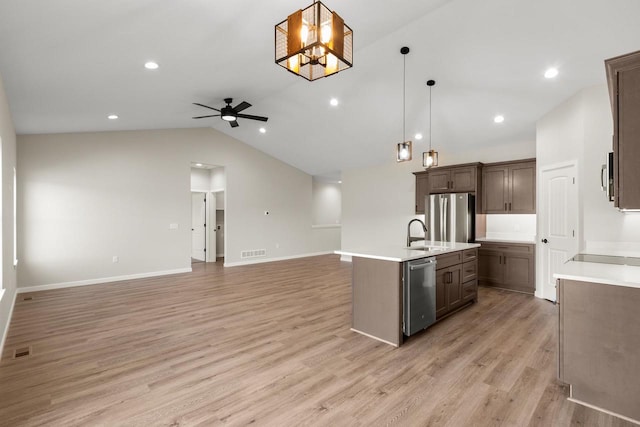 kitchen featuring lofted ceiling, stainless steel appliances, hanging light fixtures, and an island with sink