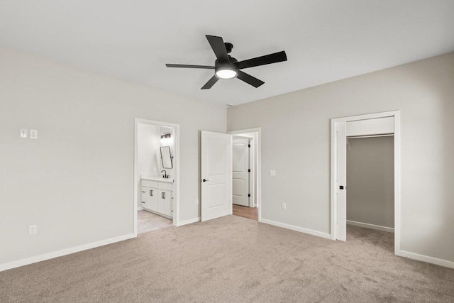 unfurnished bedroom featuring a spacious closet, ensuite bath, a closet, ceiling fan, and light colored carpet