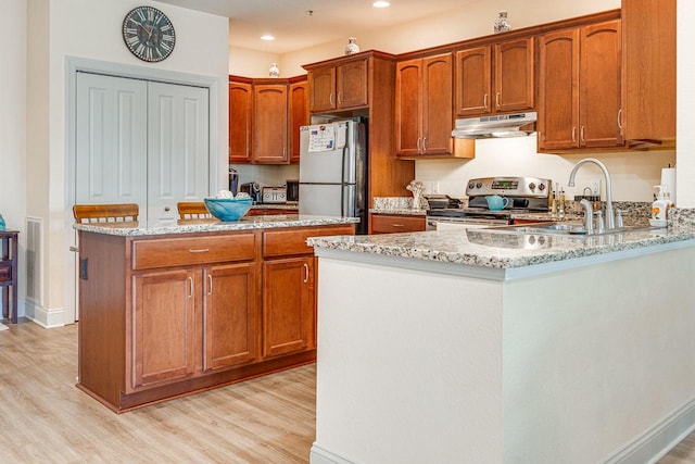 kitchen with stainless steel appliances, sink, a center island, light stone countertops, and light wood-type flooring