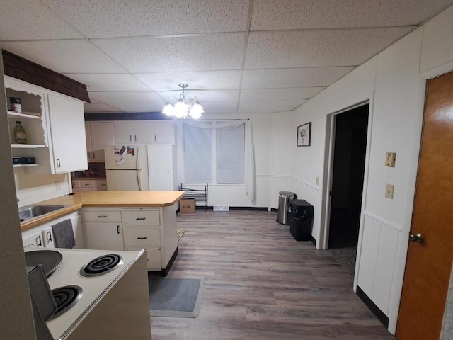 kitchen featuring a paneled ceiling, stove, hardwood / wood-style flooring, white fridge, and white cabinetry