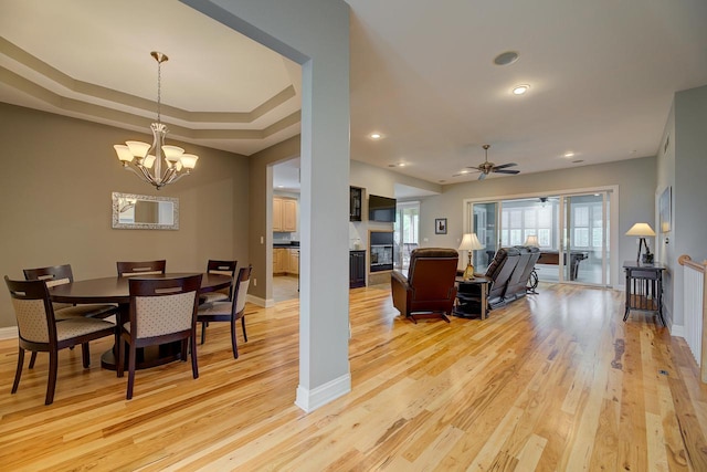 dining room featuring light hardwood / wood-style floors, a tray ceiling, and ceiling fan with notable chandelier