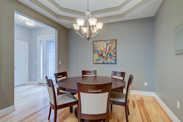 dining area featuring a raised ceiling, light hardwood / wood-style flooring, and an inviting chandelier