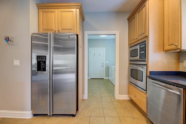 kitchen with washing machine and dryer, dark stone counters, stainless steel appliances, and light tile patterned floors