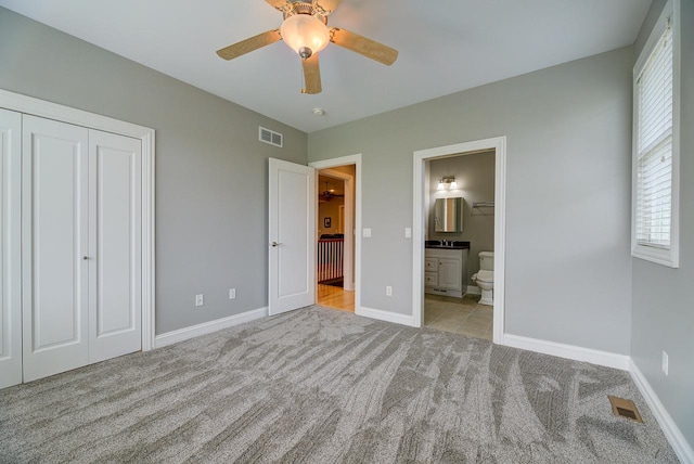 unfurnished bedroom featuring light carpet, a closet, ensuite bath, and ceiling fan