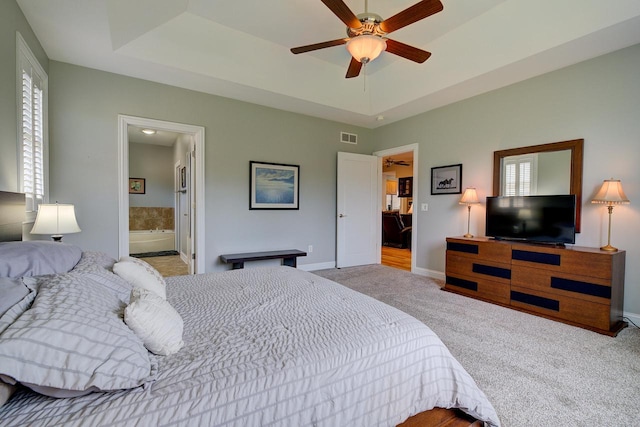 bedroom with connected bathroom, light carpet, a tray ceiling, and ceiling fan