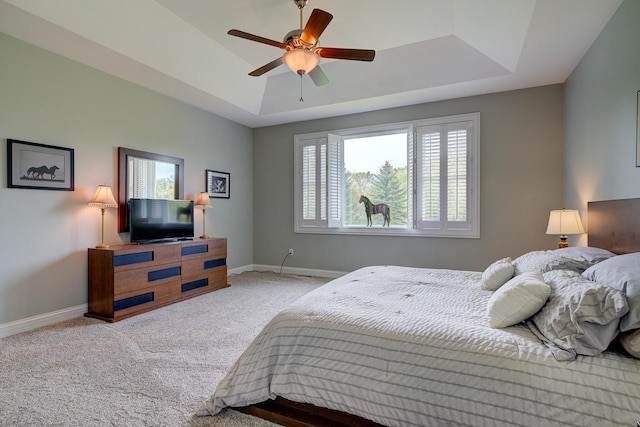 carpeted bedroom featuring ceiling fan, a tray ceiling, and multiple windows