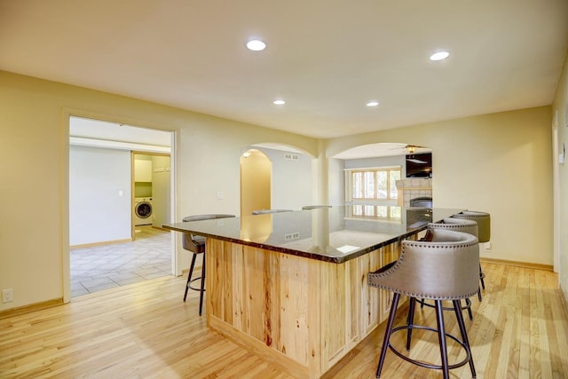 kitchen with washer / dryer, light brown cabinetry, a kitchen bar, a fireplace, and light hardwood / wood-style floors