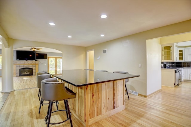 kitchen with a kitchen breakfast bar, white cabinets, a tiled fireplace, and light hardwood / wood-style floors