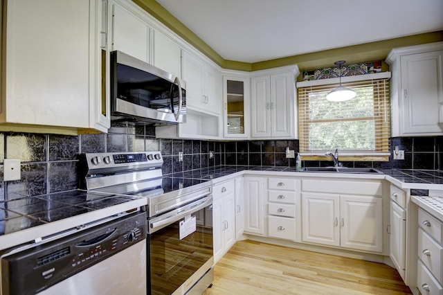 kitchen featuring decorative backsplash, white cabinets, light wood-type flooring, sink, and stainless steel appliances