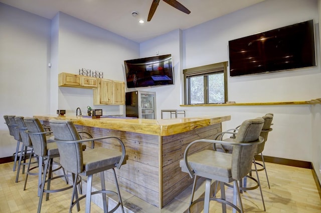 bar featuring stainless steel refrigerator, light brown cabinets, light hardwood / wood-style floors, and ceiling fan