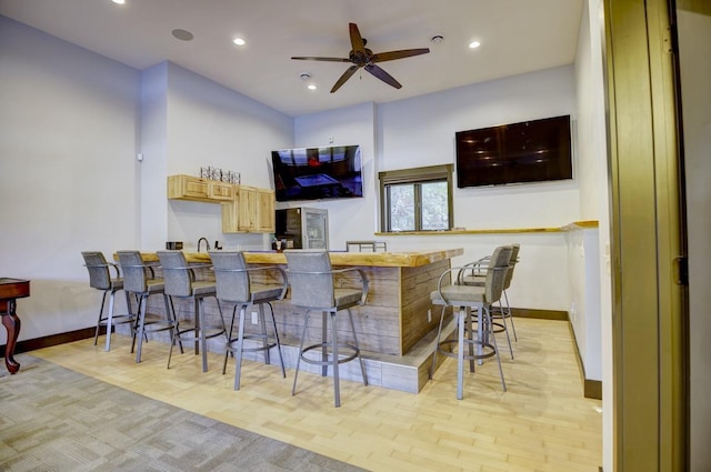 bar with light hardwood / wood-style floors, light brown cabinets, and ceiling fan