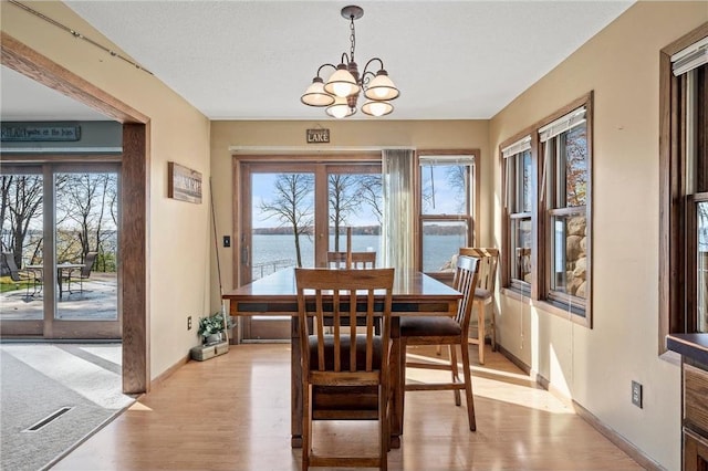 dining space featuring light hardwood / wood-style floors, a chandelier, a textured ceiling, and a water view