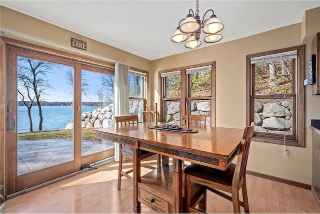 dining area featuring a textured ceiling, light hardwood / wood-style floors, a water view, and a chandelier