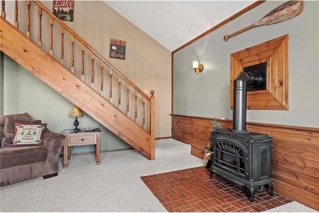 living room featuring wood walls, high vaulted ceiling, a wood stove, and dark carpet