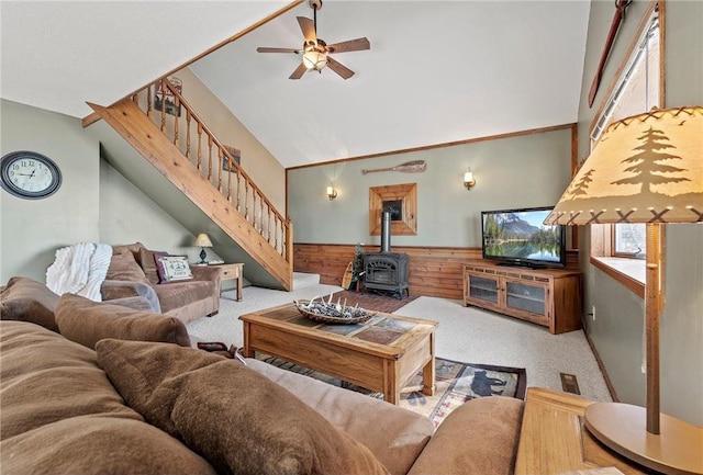 carpeted living room with a wood stove, high vaulted ceiling, wooden walls, and ceiling fan