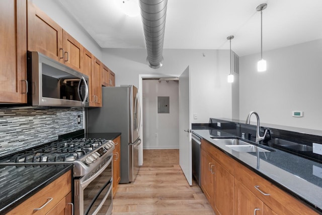 kitchen with appliances with stainless steel finishes, dark stone counters, light wood-type flooring, pendant lighting, and sink