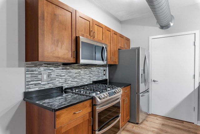 kitchen featuring appliances with stainless steel finishes, decorative backsplash, dark stone countertops, and light hardwood / wood-style floors