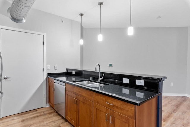 kitchen with hanging light fixtures, dark stone counters, sink, stainless steel dishwasher, and light hardwood / wood-style floors