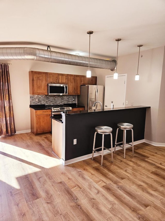 kitchen featuring hanging light fixtures, stainless steel appliances, light hardwood / wood-style floors, and kitchen peninsula