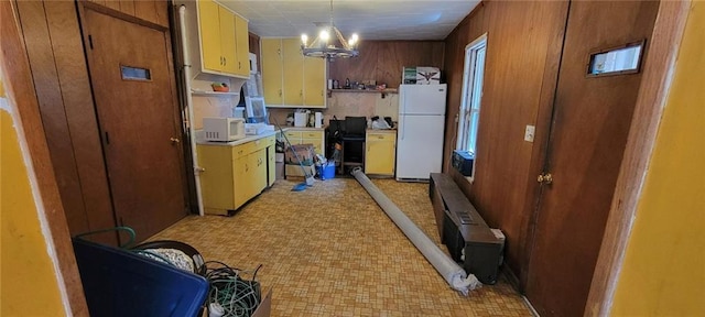 kitchen with light floors, wood walls, light countertops, a notable chandelier, and white appliances