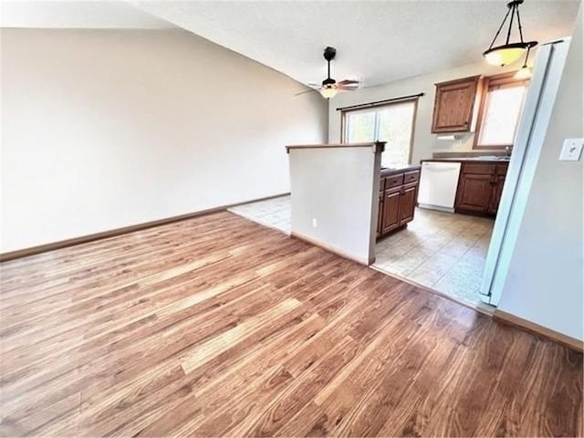 kitchen featuring white dishwasher, light hardwood / wood-style floors, ceiling fan, vaulted ceiling, and pendant lighting