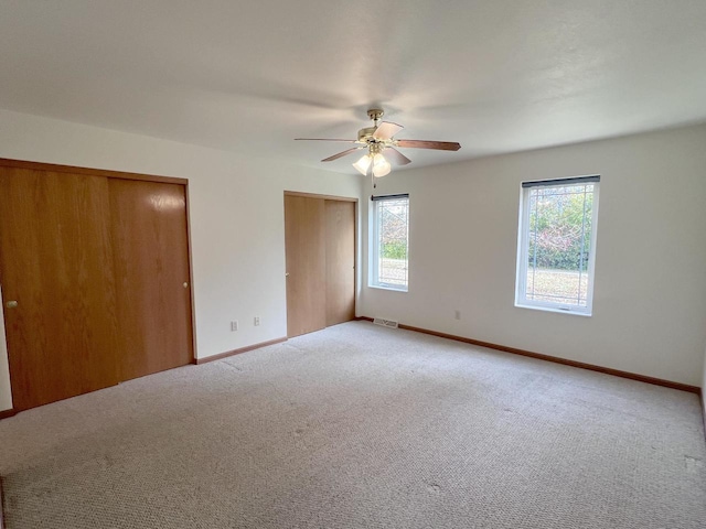 unfurnished bedroom with two closets, light colored carpet, and ceiling fan