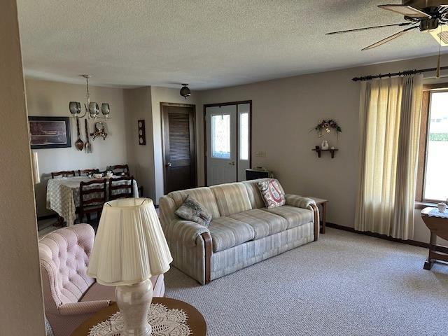 carpeted living room featuring a wealth of natural light, a textured ceiling, and ceiling fan with notable chandelier