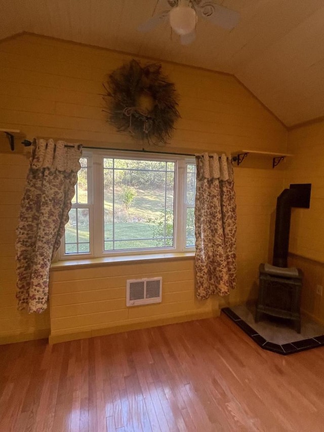 unfurnished living room featuring lofted ceiling, ceiling fan, wood-type flooring, wood walls, and a wood stove