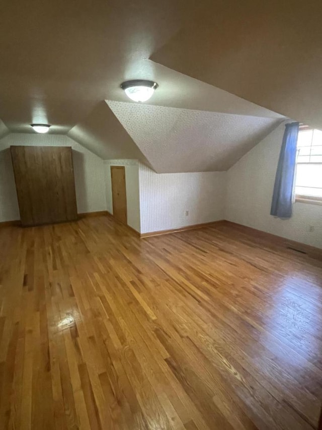 additional living space with vaulted ceiling, a textured ceiling, and light hardwood / wood-style floors