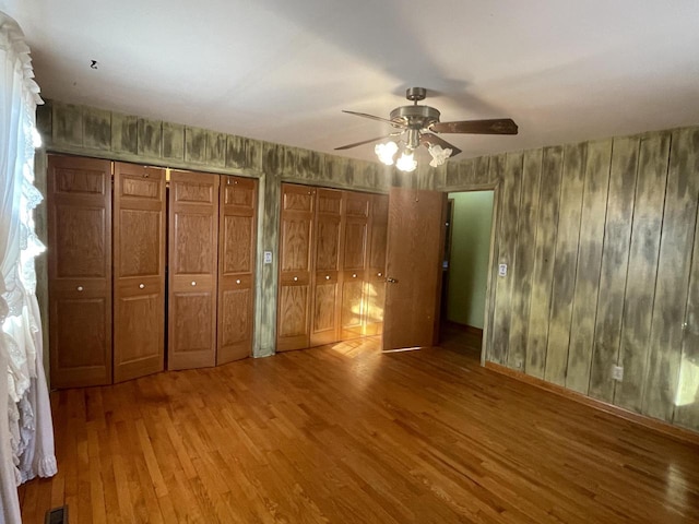 unfurnished bedroom with ceiling fan, multiple closets, and hardwood / wood-style floors