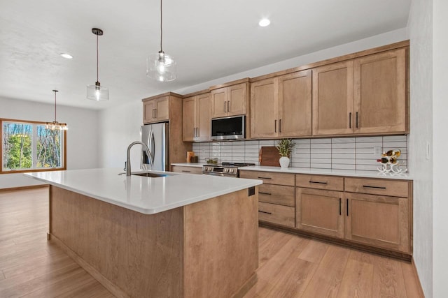 kitchen with tasteful backsplash, appliances with stainless steel finishes, light hardwood / wood-style floors, pendant lighting, and a kitchen island with sink