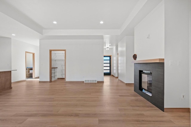 unfurnished living room featuring visible vents, baseboards, recessed lighting, a multi sided fireplace, and light wood-style flooring