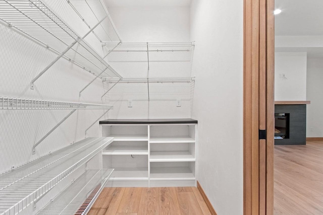 spacious closet featuring a glass covered fireplace and wood finished floors