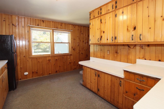 kitchen with light countertops, carpet flooring, wood walls, and freestanding refrigerator