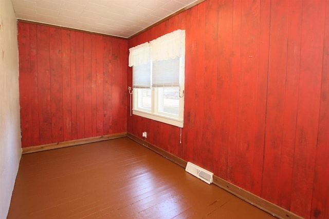 empty room featuring visible vents, wood-type flooring, wooden walls, and baseboards