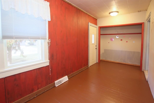 unfurnished room with visible vents, wood walls, and wood finished floors