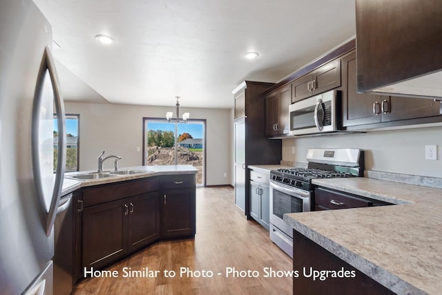 kitchen featuring hanging light fixtures, stainless steel appliances, sink, an inviting chandelier, and light hardwood / wood-style floors