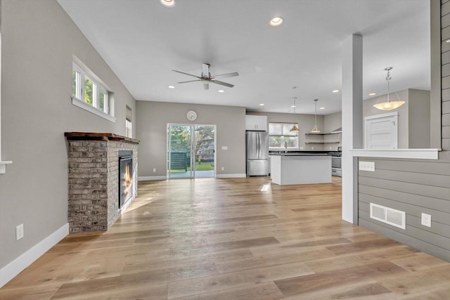 unfurnished living room featuring a fireplace, light wood-type flooring, and ceiling fan