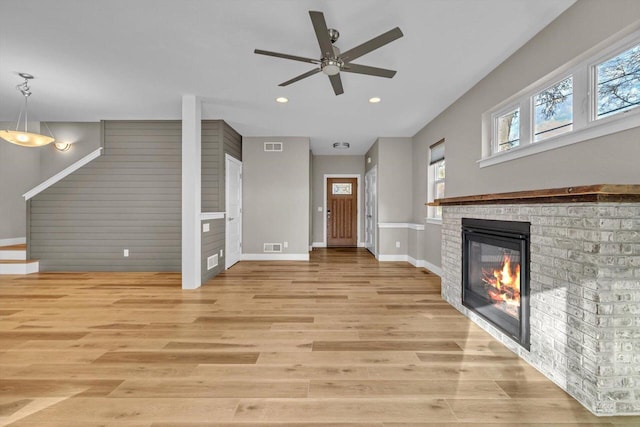 unfurnished living room featuring ceiling fan, light wood-type flooring, and a brick fireplace