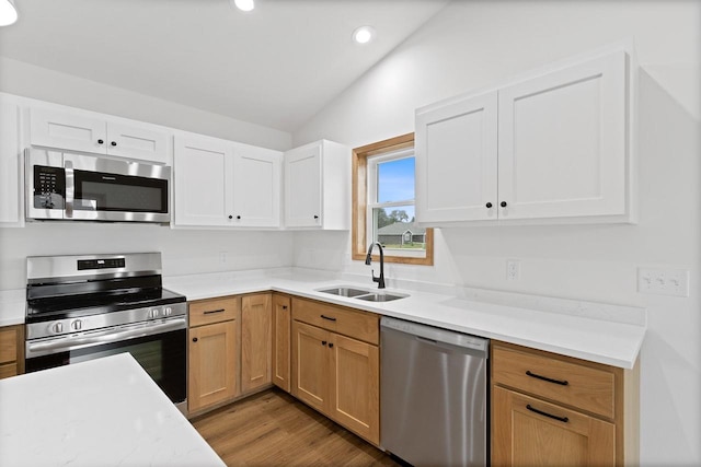 kitchen with wood-type flooring, sink, white cabinetry, stainless steel appliances, and vaulted ceiling